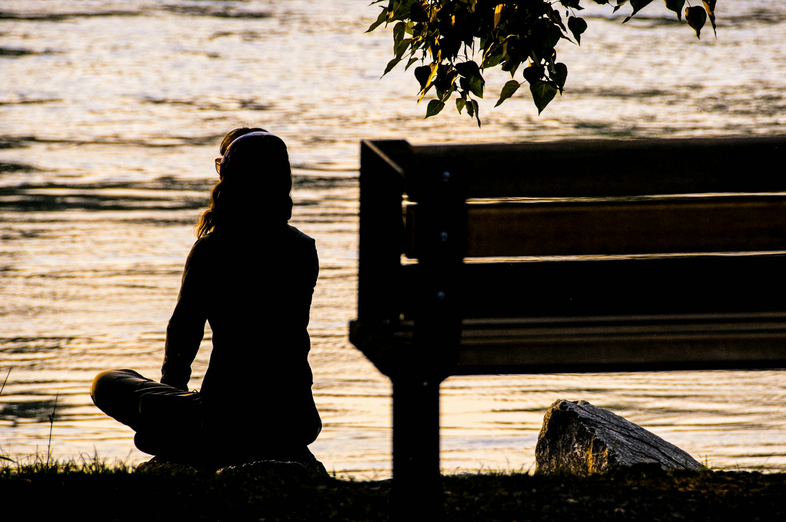 Silhouette of person sitting peacefully near bench near body of water during daytime